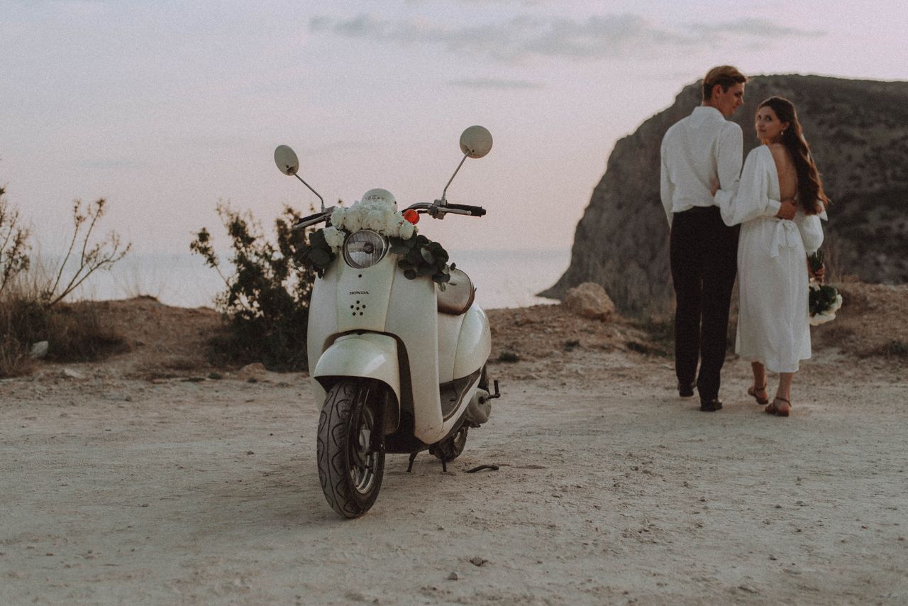 A couple enjoys a romantic moment by a cliff with a scooter at sunset.